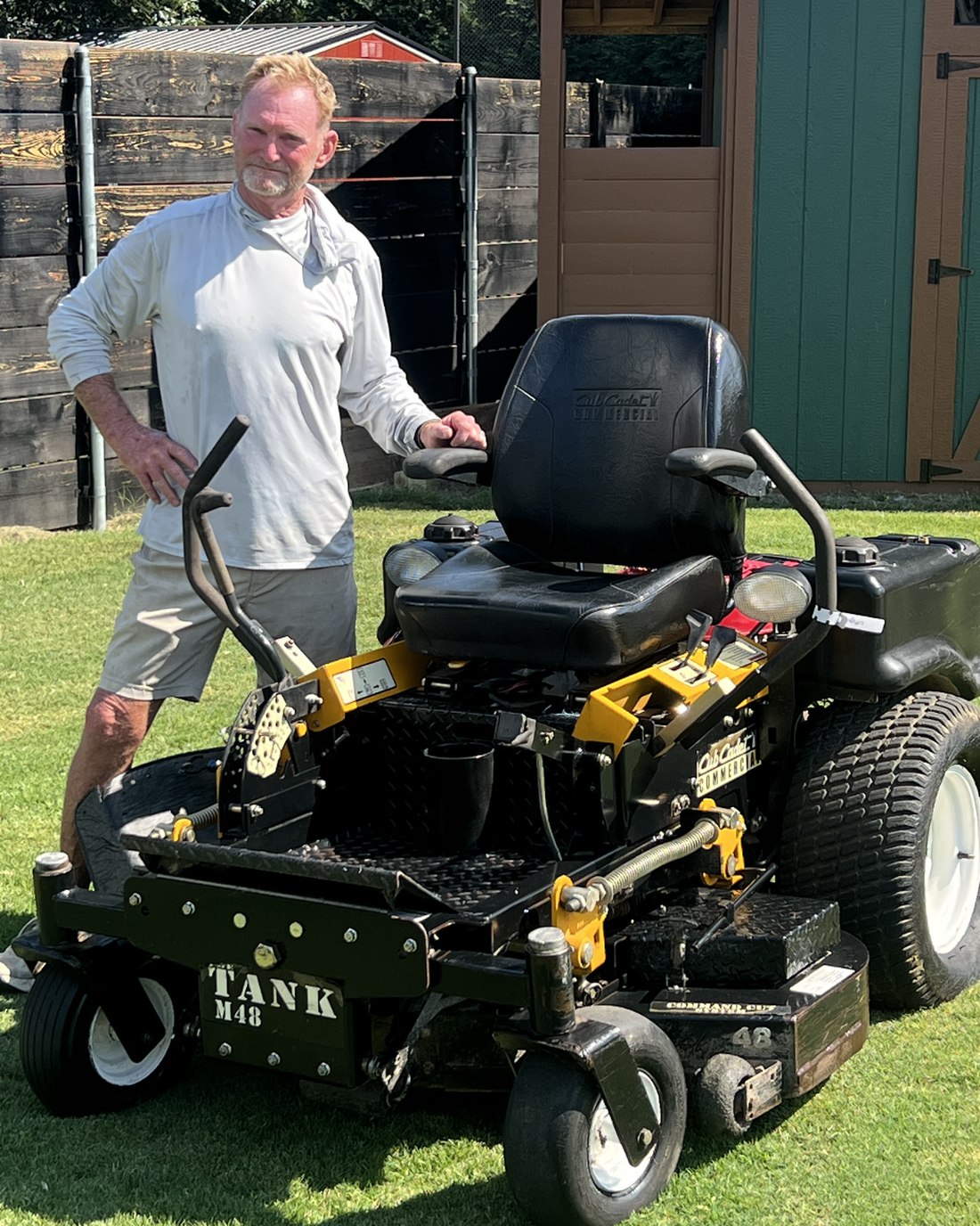 Chip Ward standing beside a commercial zero-turn mower on a cut lawn