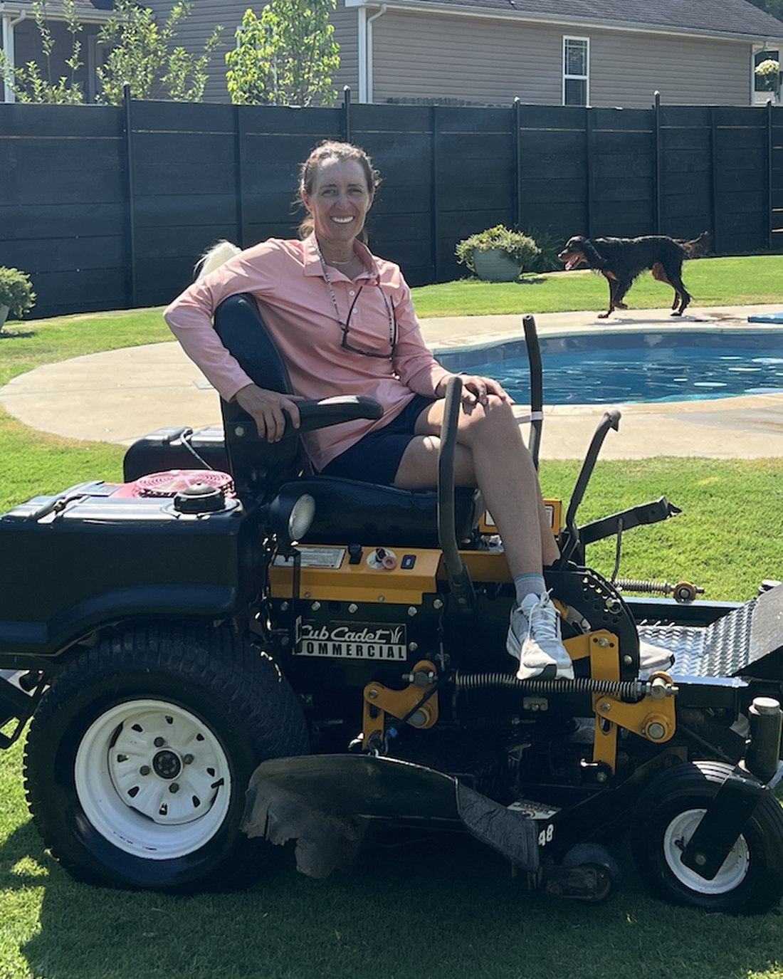 Colette Murray seated on a commercial zero-turn mower on a cut lawn