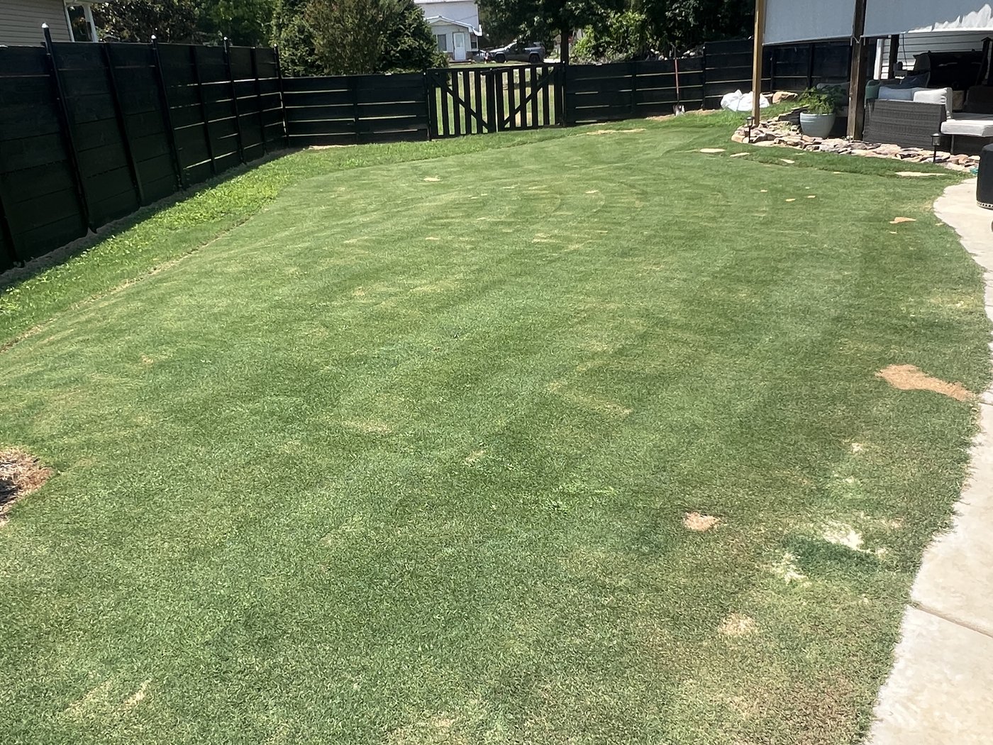 A finished back lawn of thick grass bounded by a dark fence, with a ridge line in the distance