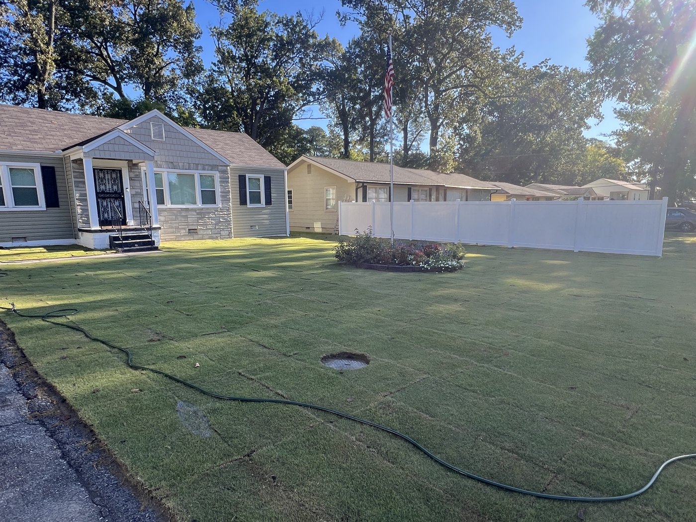 The same front lawn covered in fresh green sod, house and flagpole behind