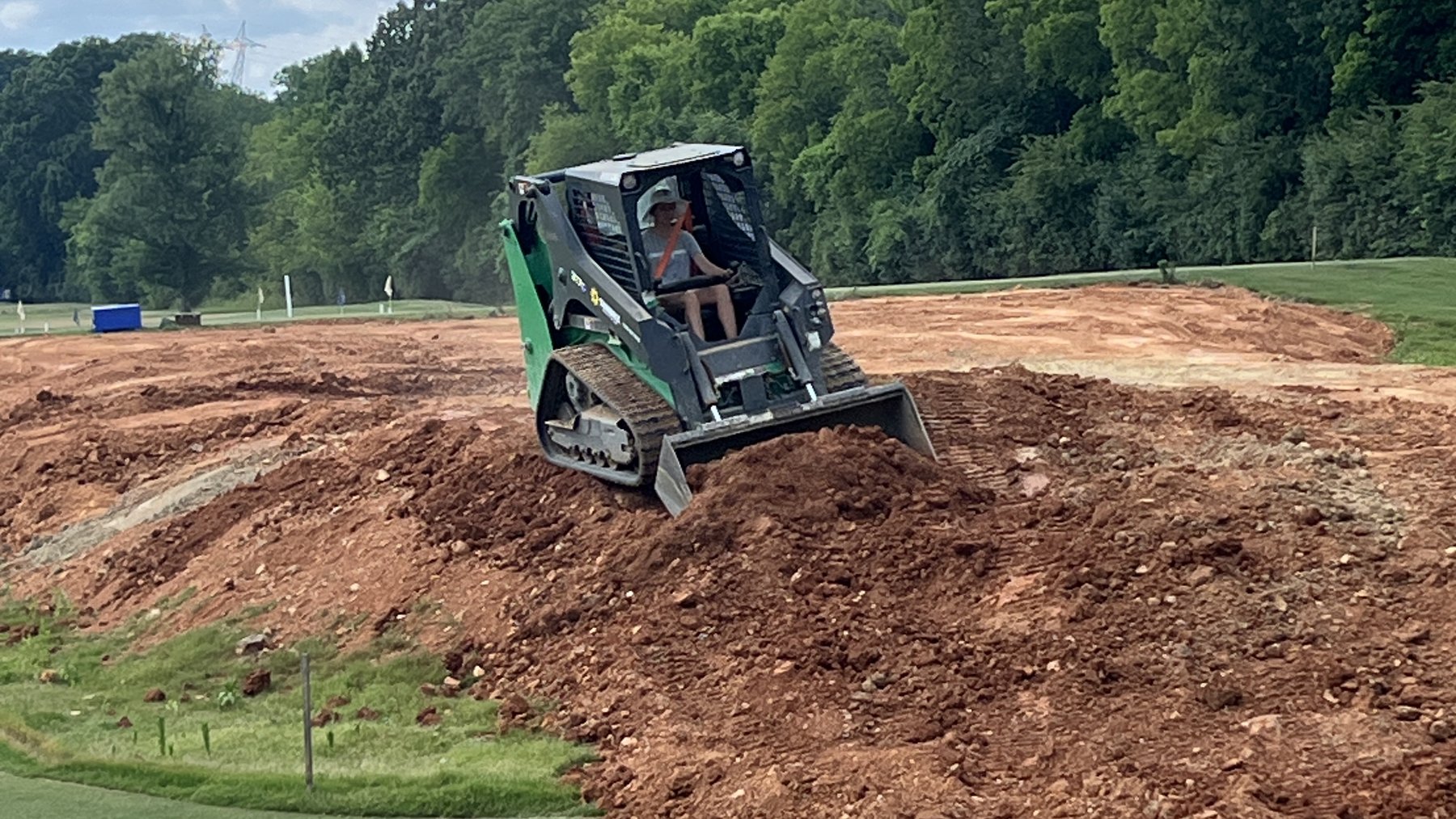 A compact track loader moving soil to reshape a slope, operated by one of the owners
