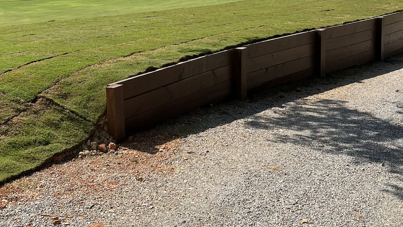 A curved timber wall holding a bank of freshly laid sod above a gravel path